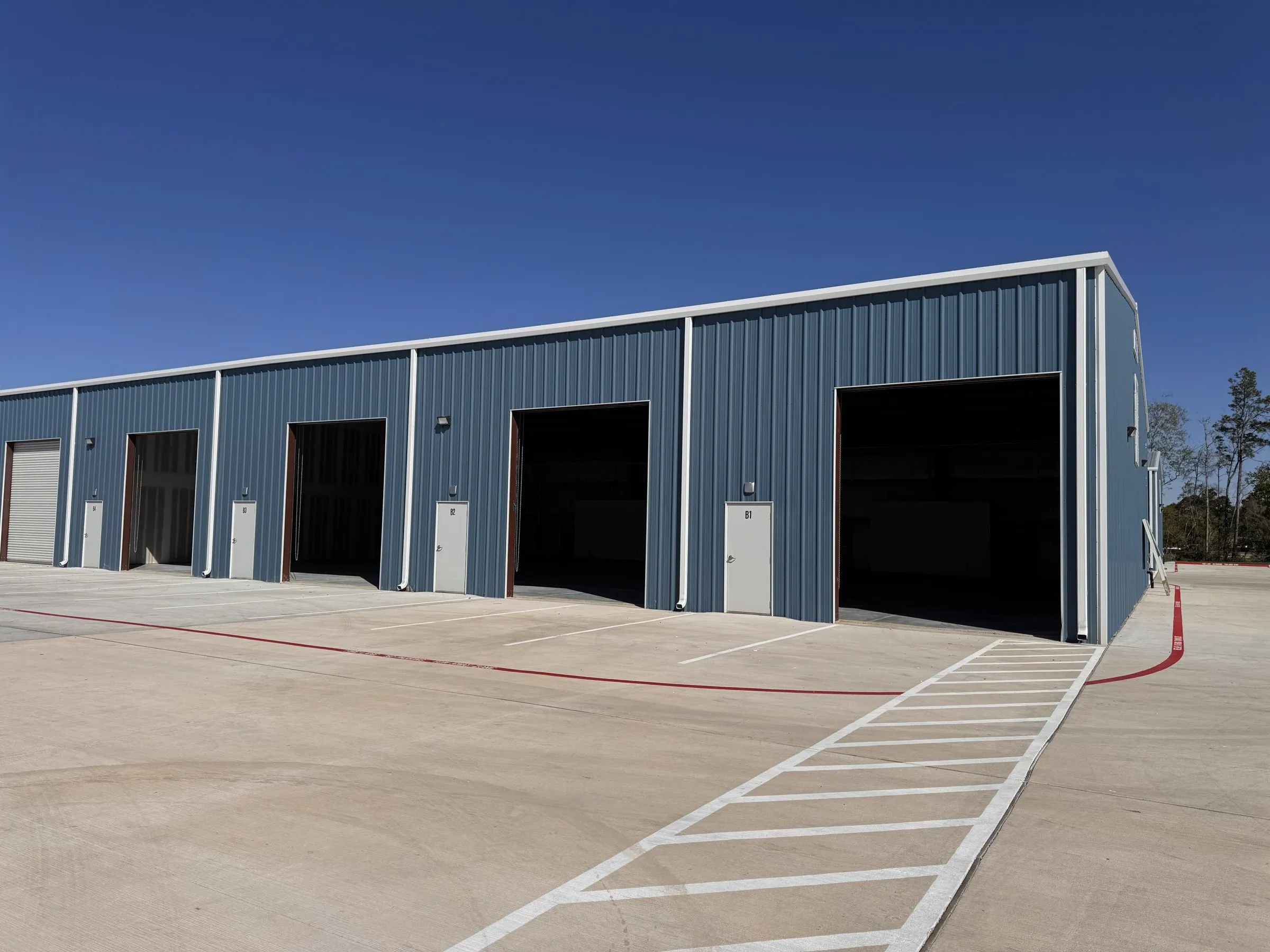 Row of grade-level roll-up doors along one of the buildings at Timber Forest Business Park, striped concrete apron in front.