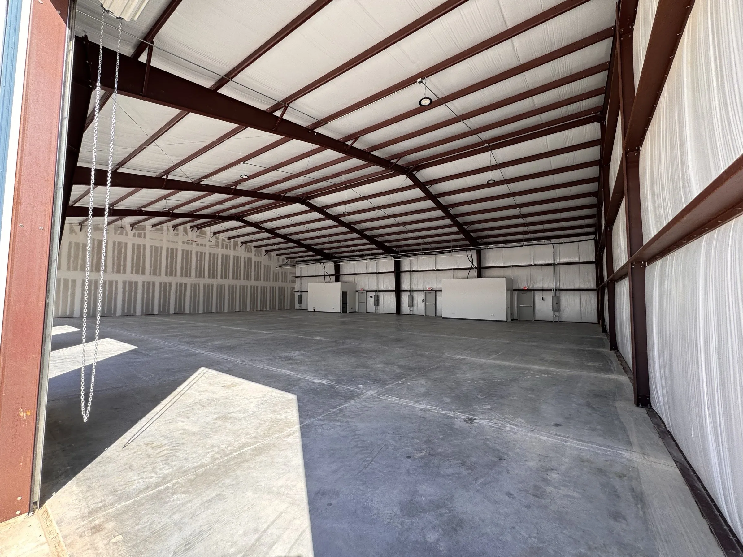 Interior steel frame and roof structure of a bay, daylight coming through the open roll-up door.