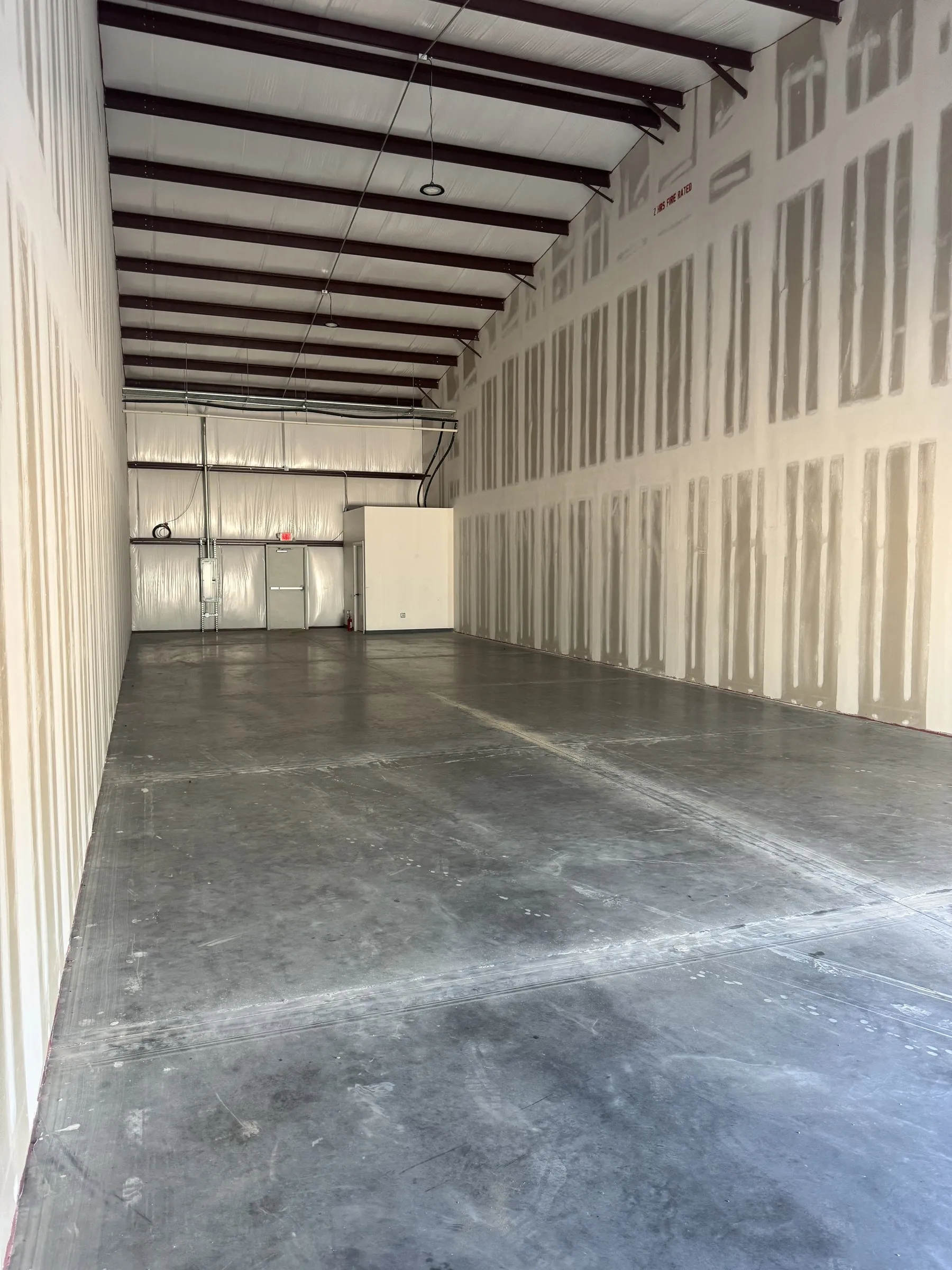 Inside an empty 2,000 SF bay: sealed concrete slab, white insulated walls and exposed steel frame to a 22 foot eave.